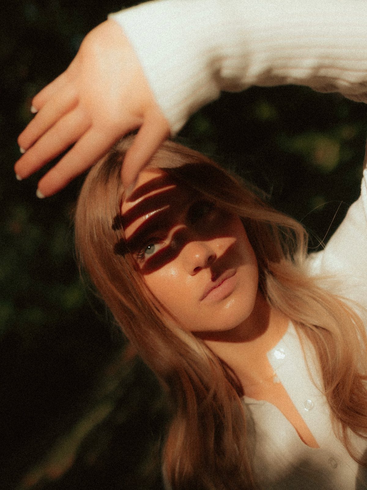 Young woman with blonde hair posing with artistic shadows across her face outdoors.