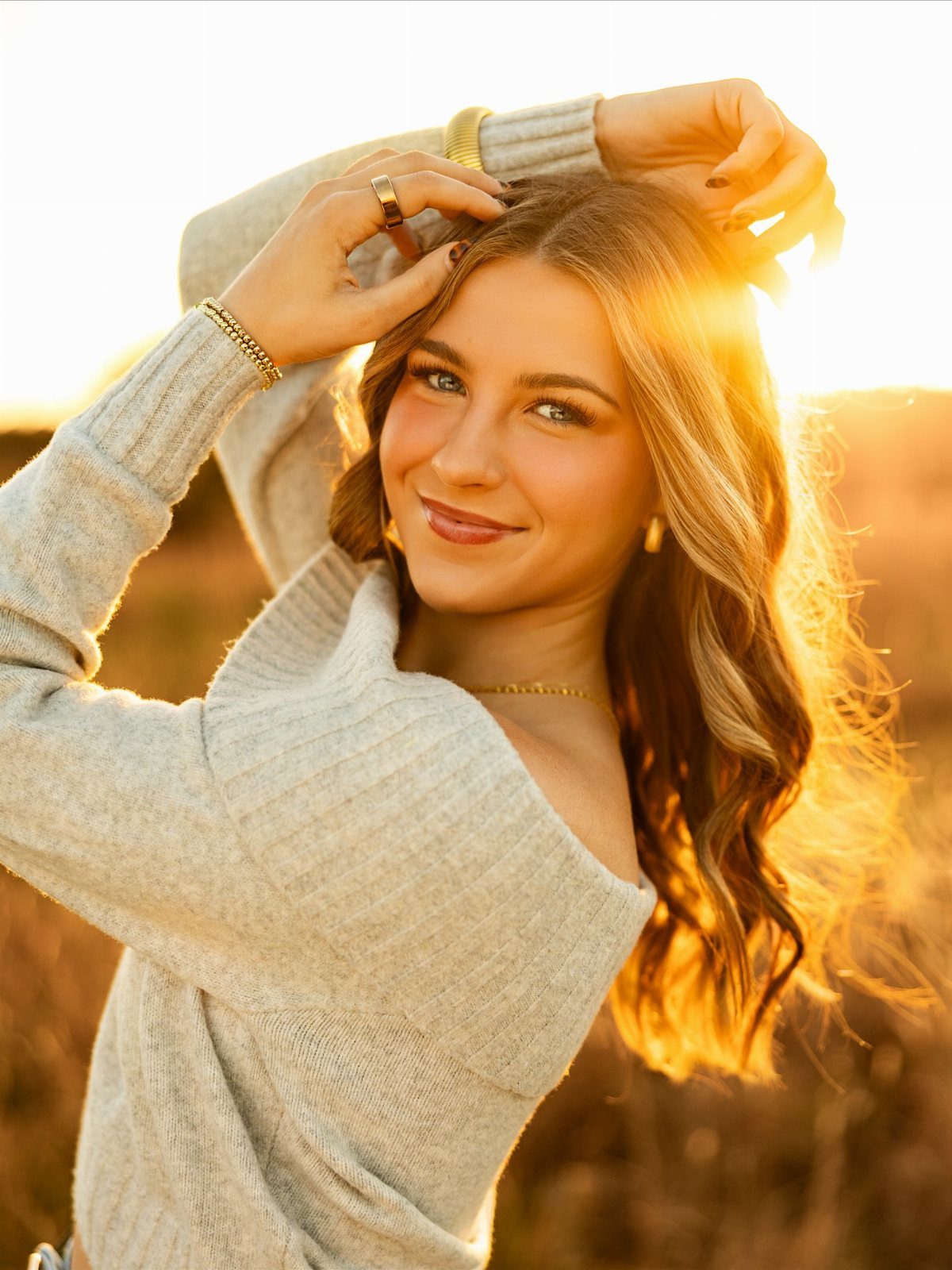 Young woman in a grey sweater posing in a field during golden hour.