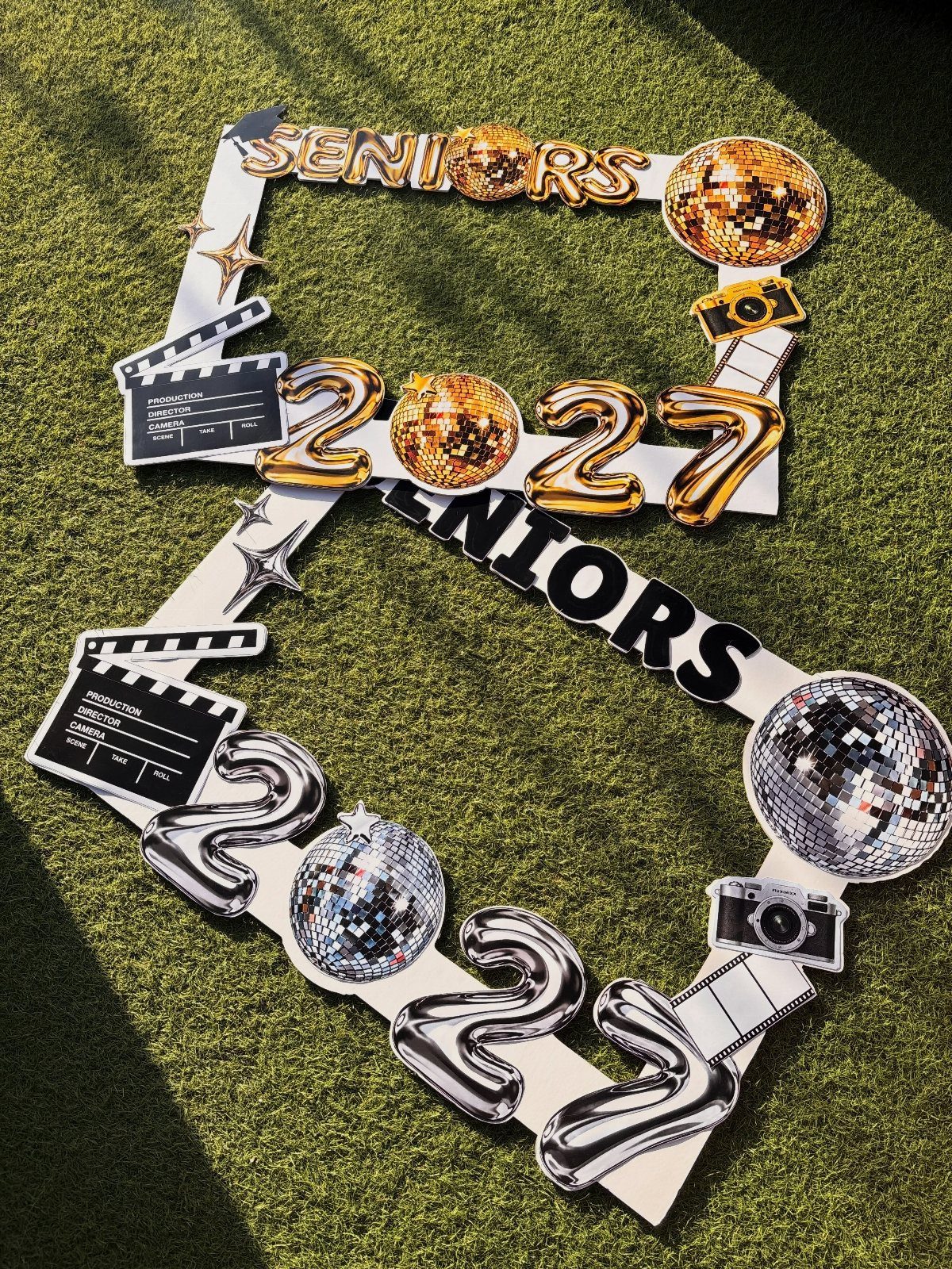 Decorative senior graduation cutout with disco balls and movie props on green grass