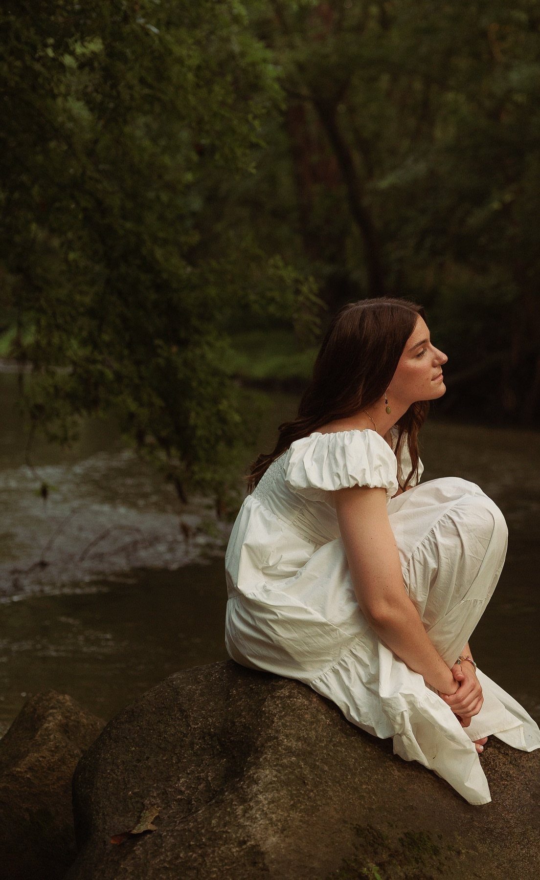 Young woman in white dress sitting on a rock by a river in nature