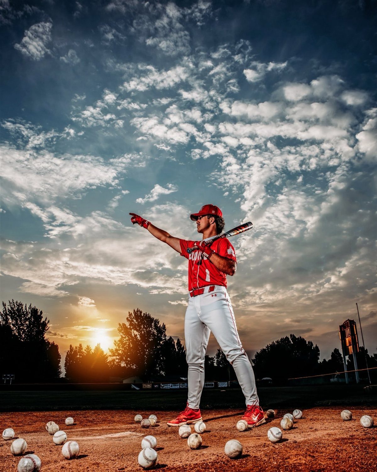 Baseball player in red uniform holding a bat on a field with baseballs