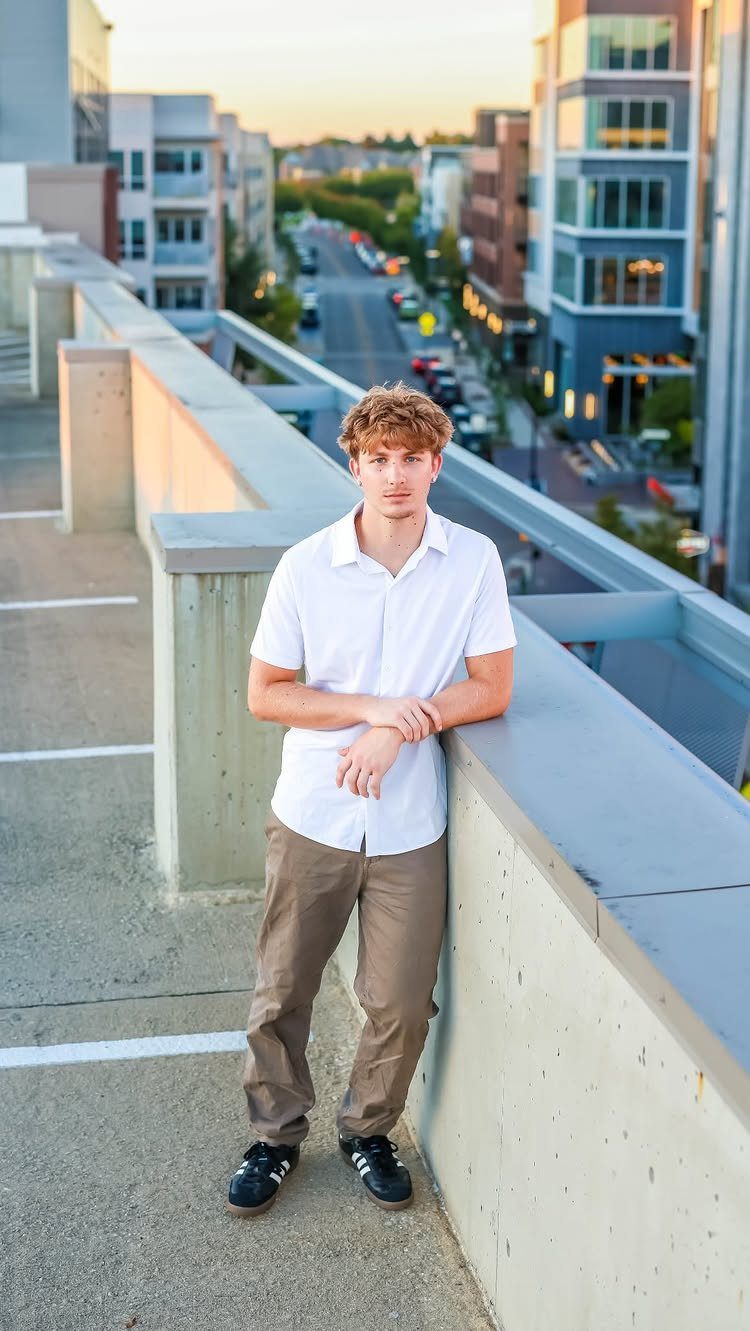 Young man in white shirt and brown pants posing on city rooftop garage.