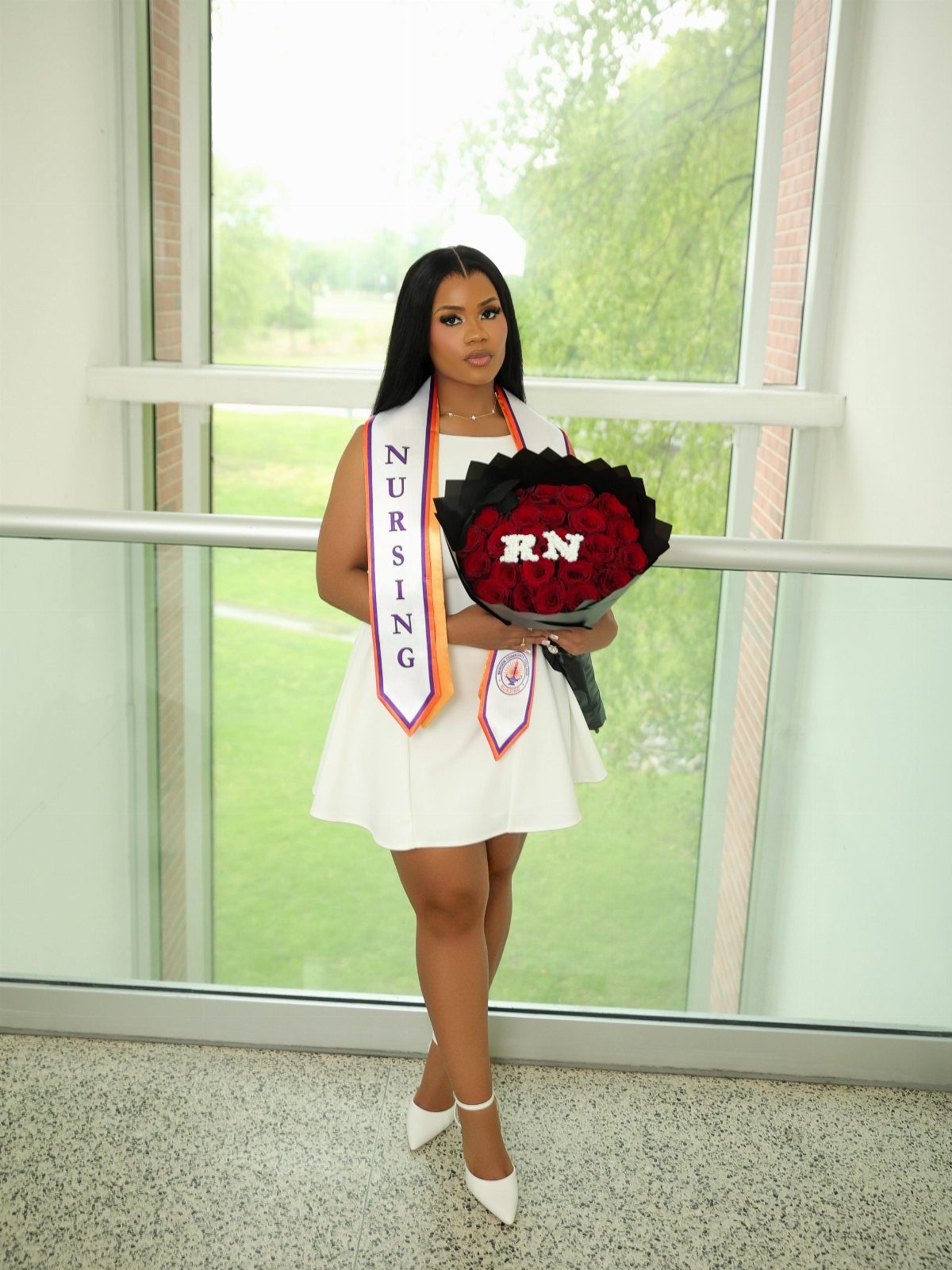 Woman in white sleeveless dress and nursing sash holding red rose bouquet