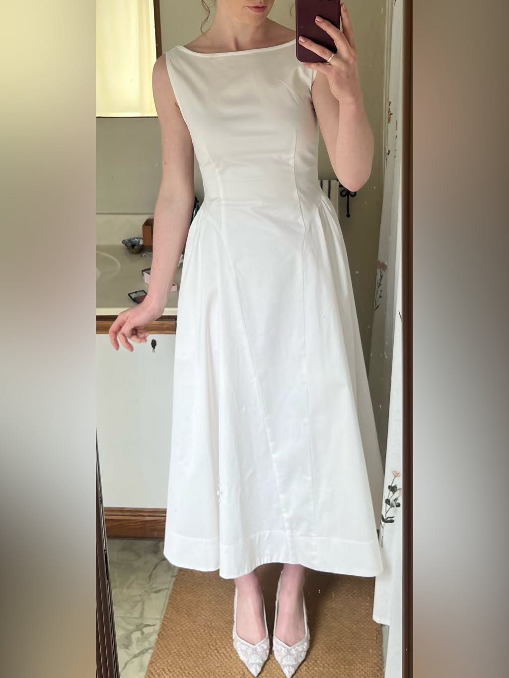Woman in a sleeveless white midi dress and white pointed-toe heels posing in mirror.