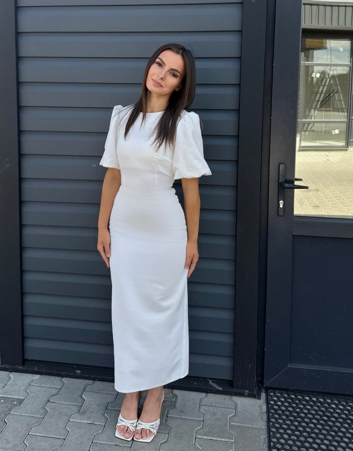 Woman wearing a white midi dress with flutter sleeves and white strappy heels.