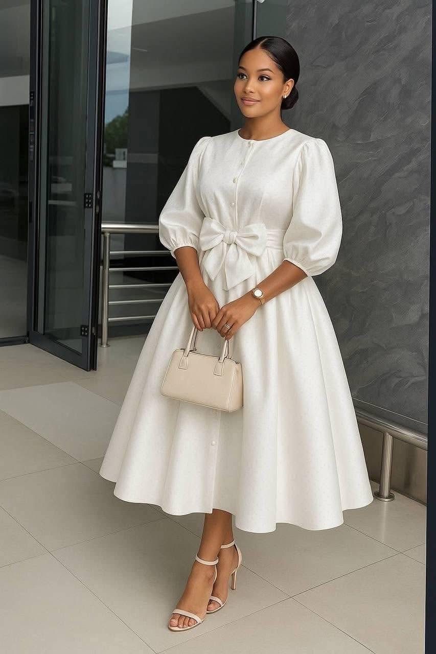 Woman in a white midi dress with puff sleeves and a waist bow.