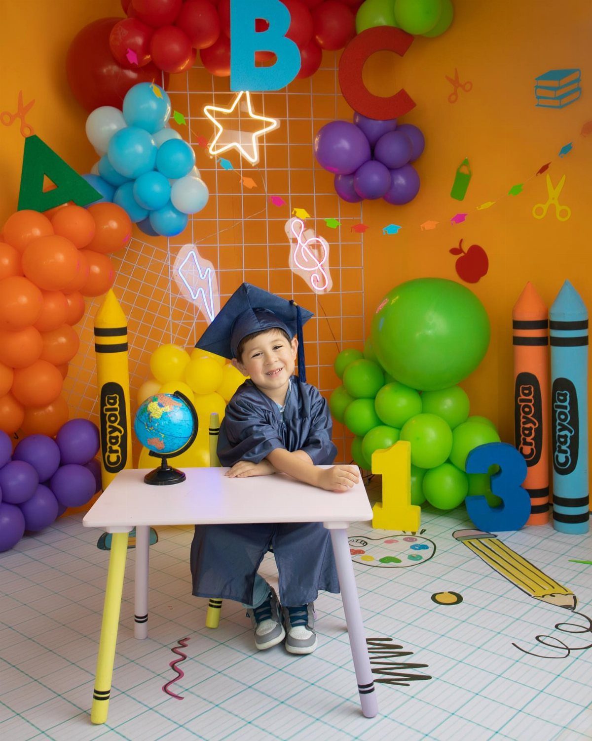 Young child in blue graduation cap and gown posing in colorful classroom set
