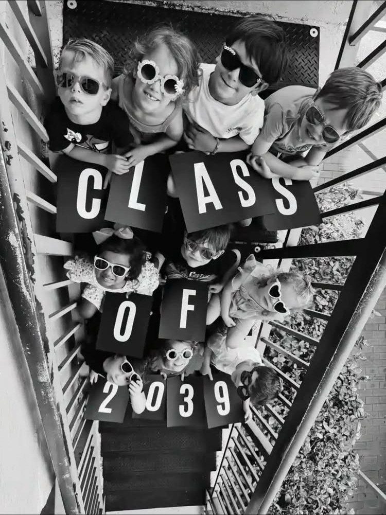 Young children in sunglasses holding signs that say Class of 2039 on stairs.