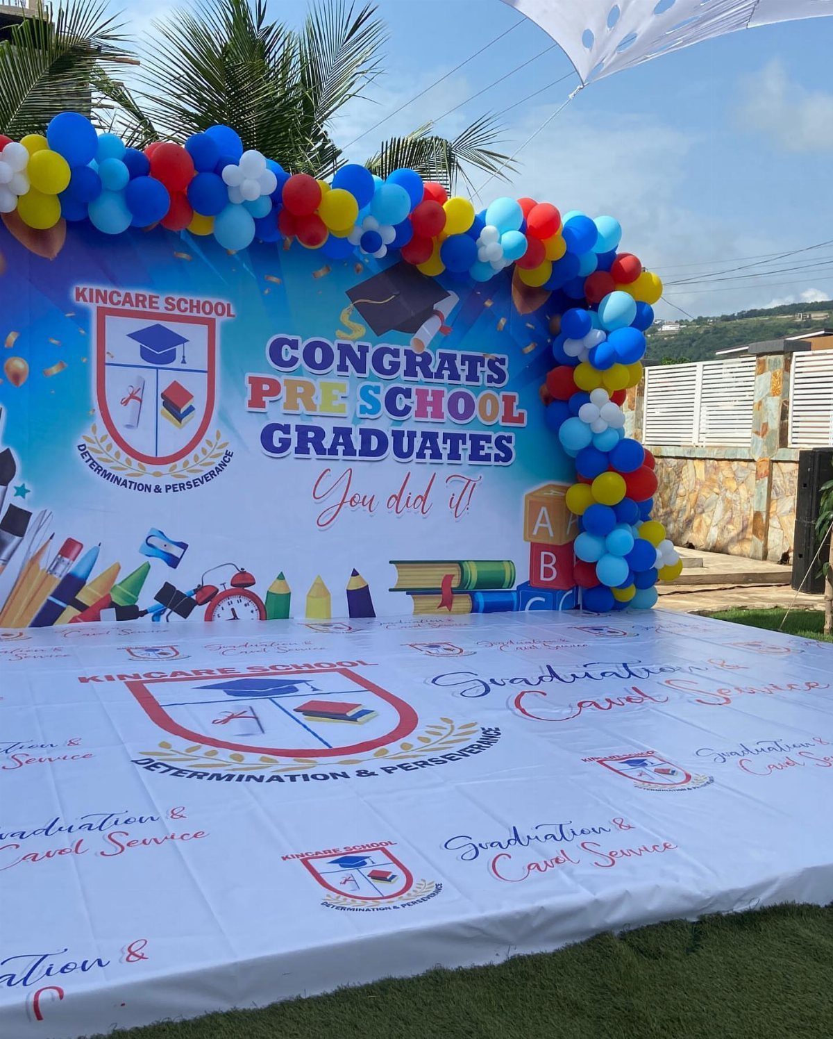 Preschool graduation backdrop with colorful balloons and congratulatory text on a grassy lawn