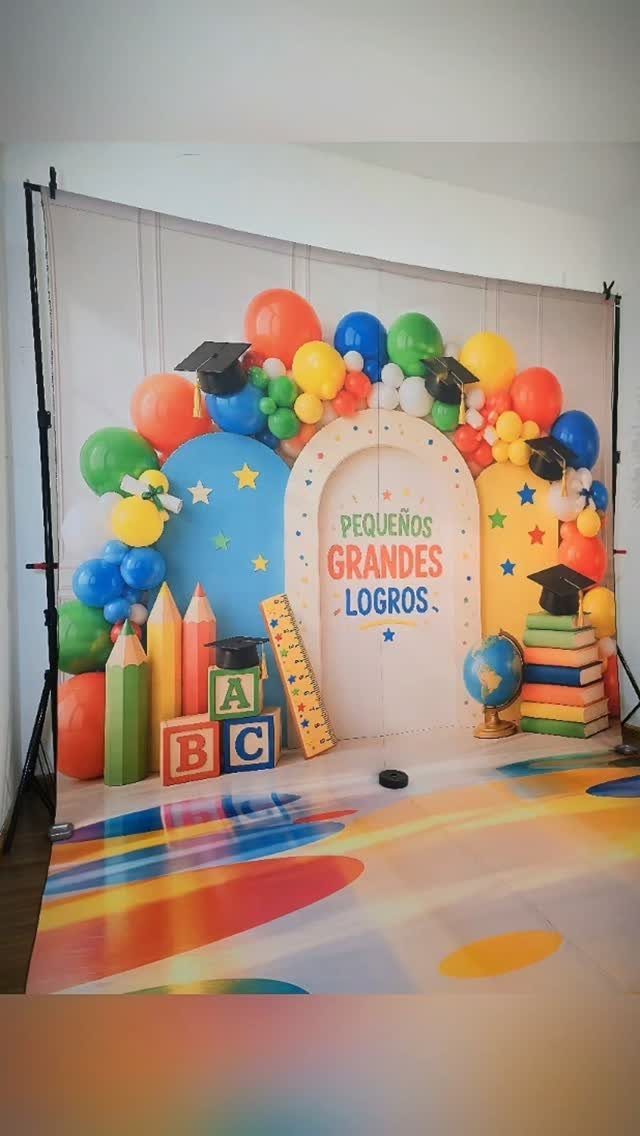Colorful graduation backdrop with balloons, giant pencils, and ABC blocks for children.