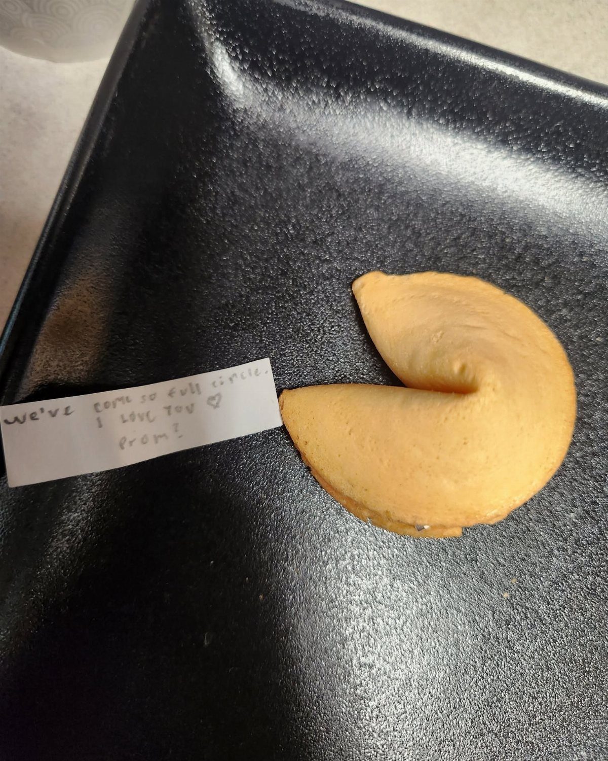 Fortune cookie and a handwritten prom invitation note on a black plate.