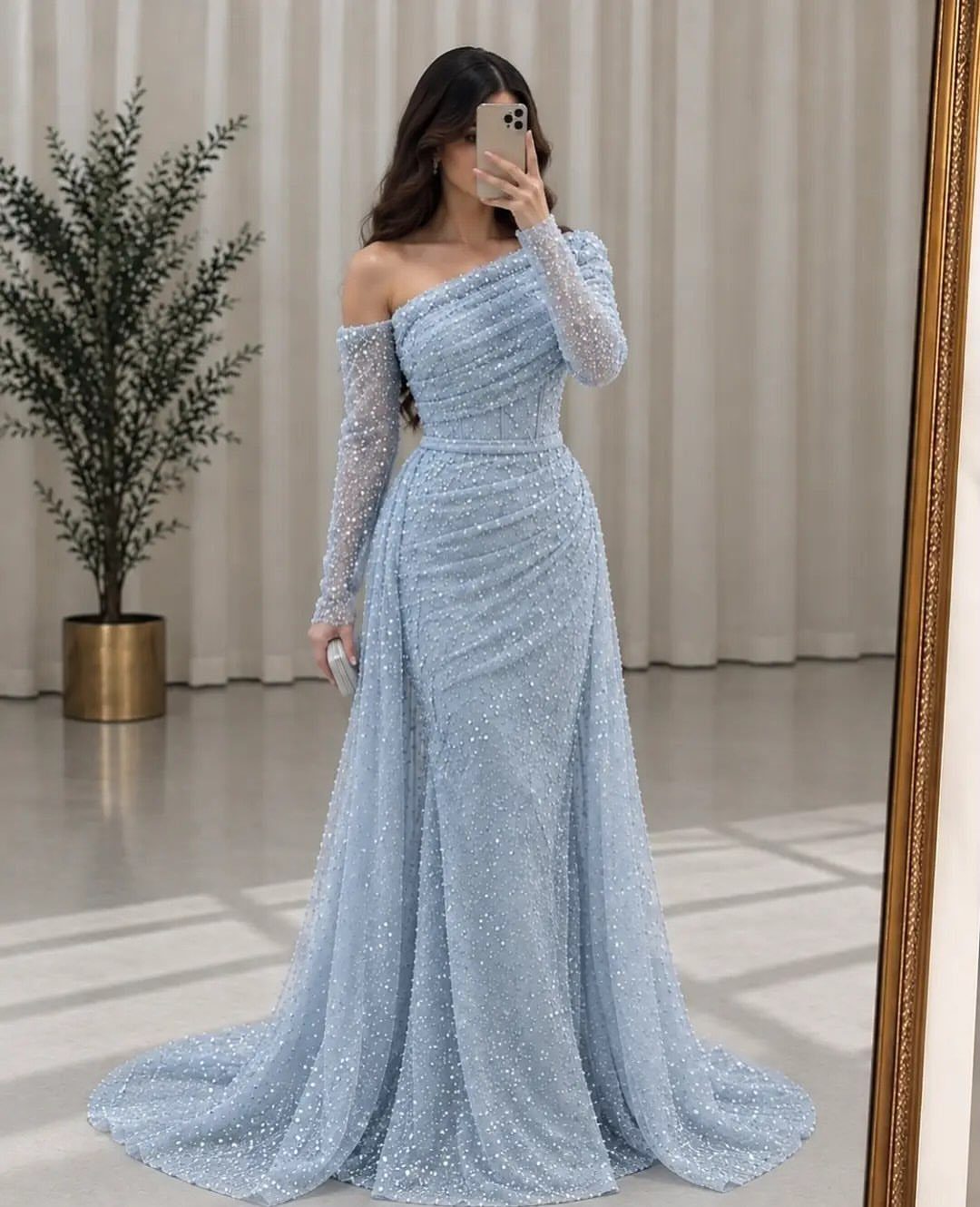 Woman in a sparkling light blue asymmetrical prom dress taking a mirror selfie.