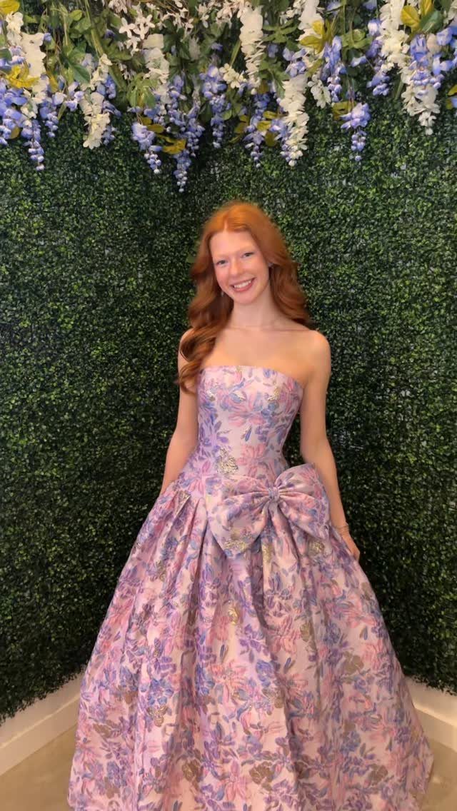 Young woman in a strapless floral prom dress posing before a flower wall