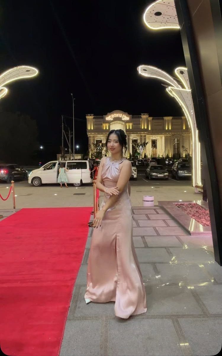 Young woman in a pale pink satin gown posing on a red carpet.