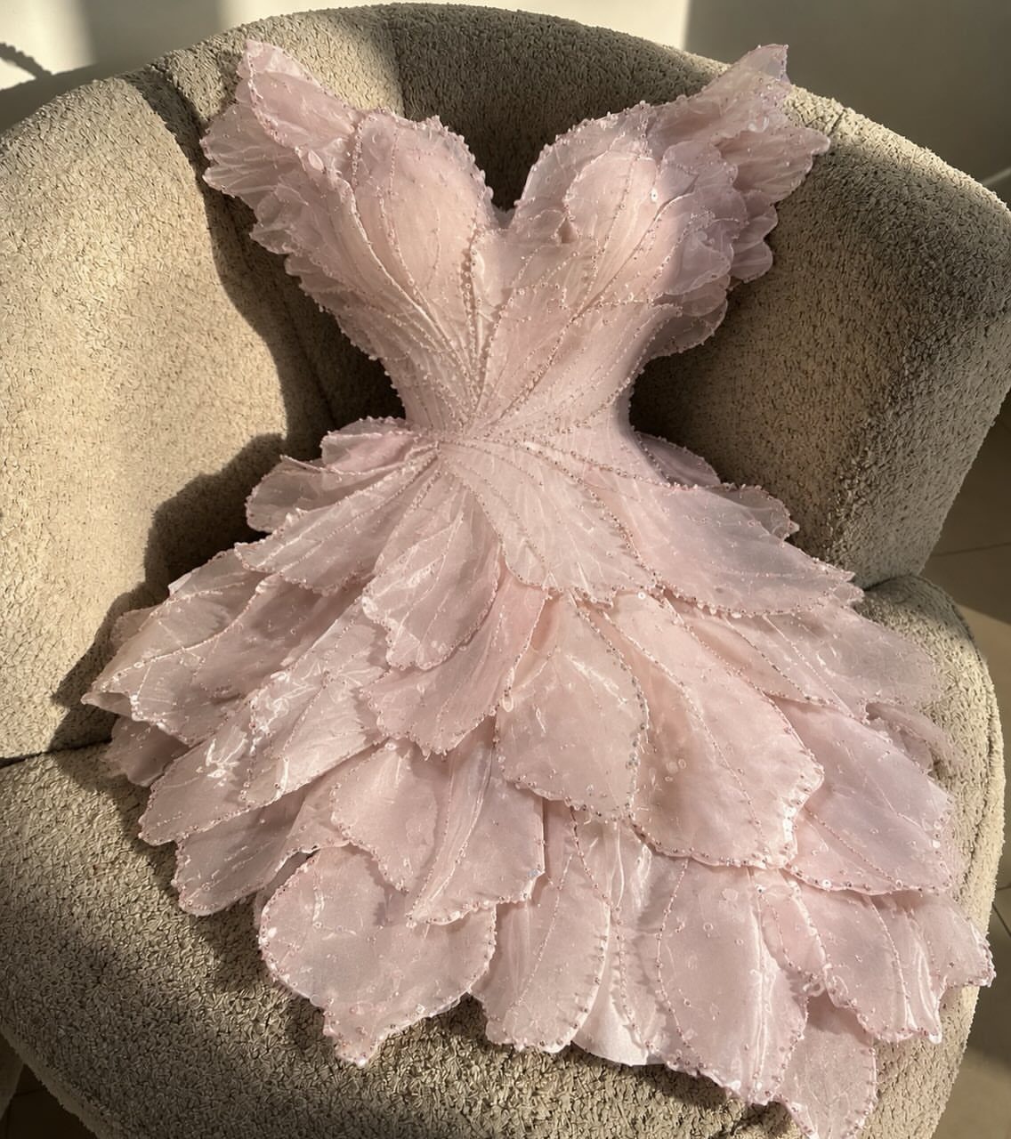 Light pink mini dress with 3D floral petal textures resting on a beige chair