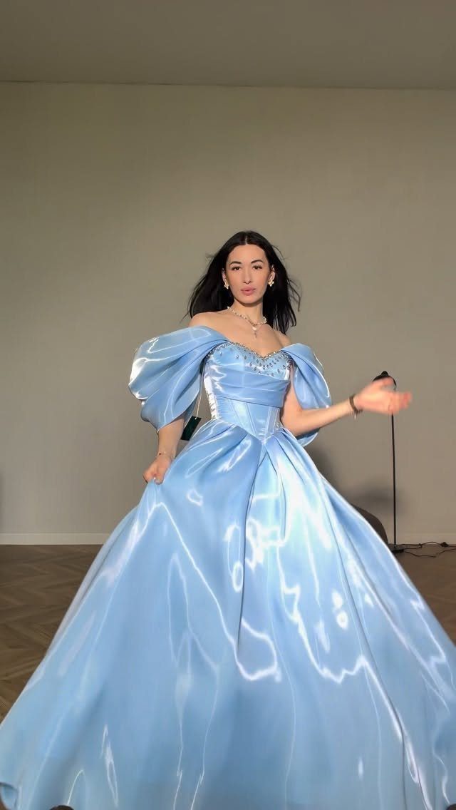 Woman wearing a voluminous light blue satin ballgown with puffed off-the-shoulder sleeves.