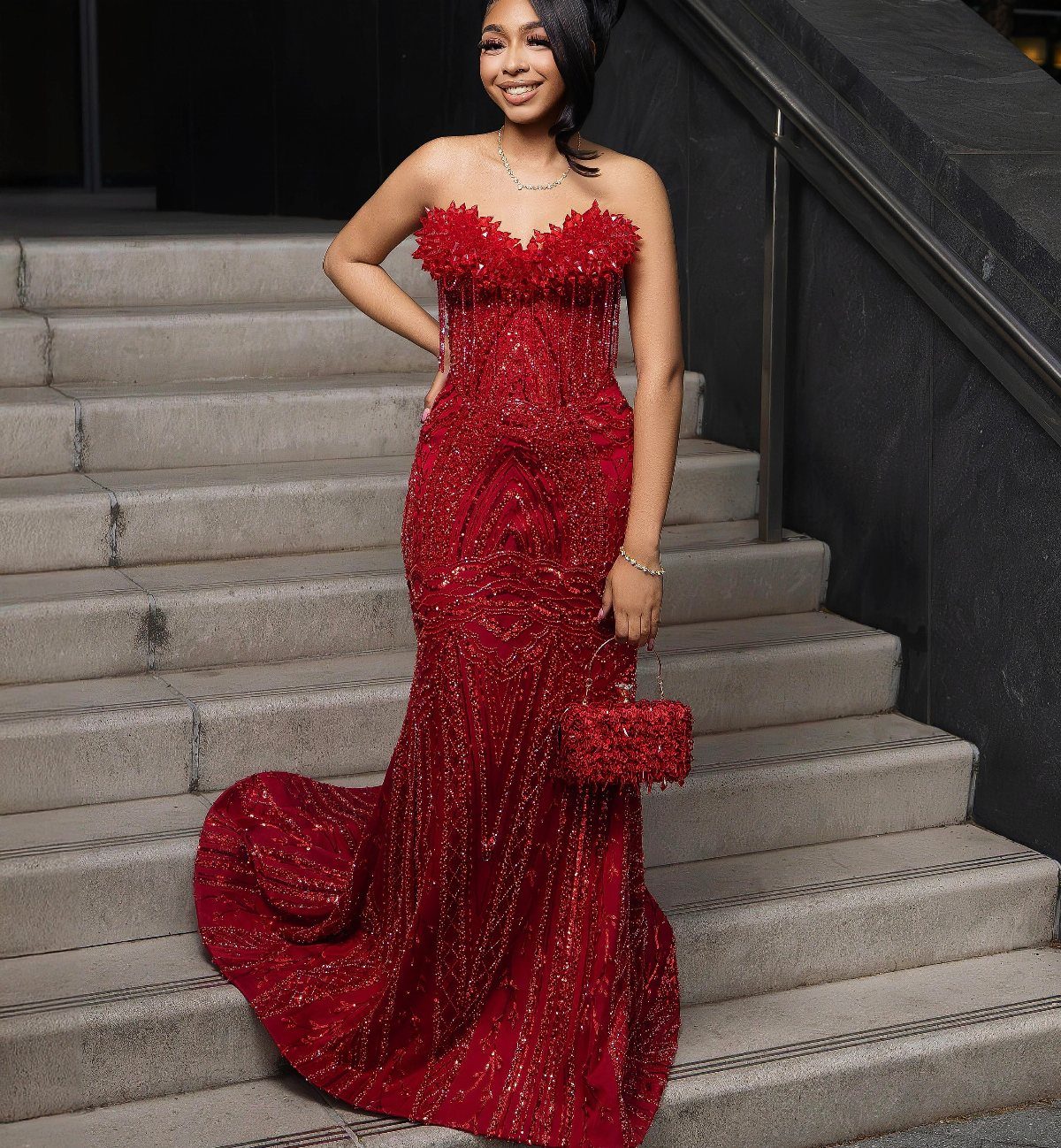 Woman in a strapless red sequined prom dress standing on concrete stairs.