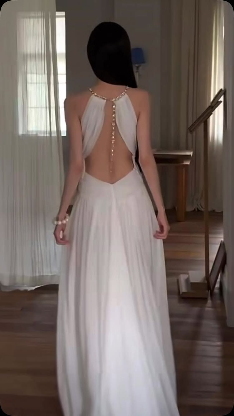 Woman from behind wearing a white halter maxi dress with pearl back detail.