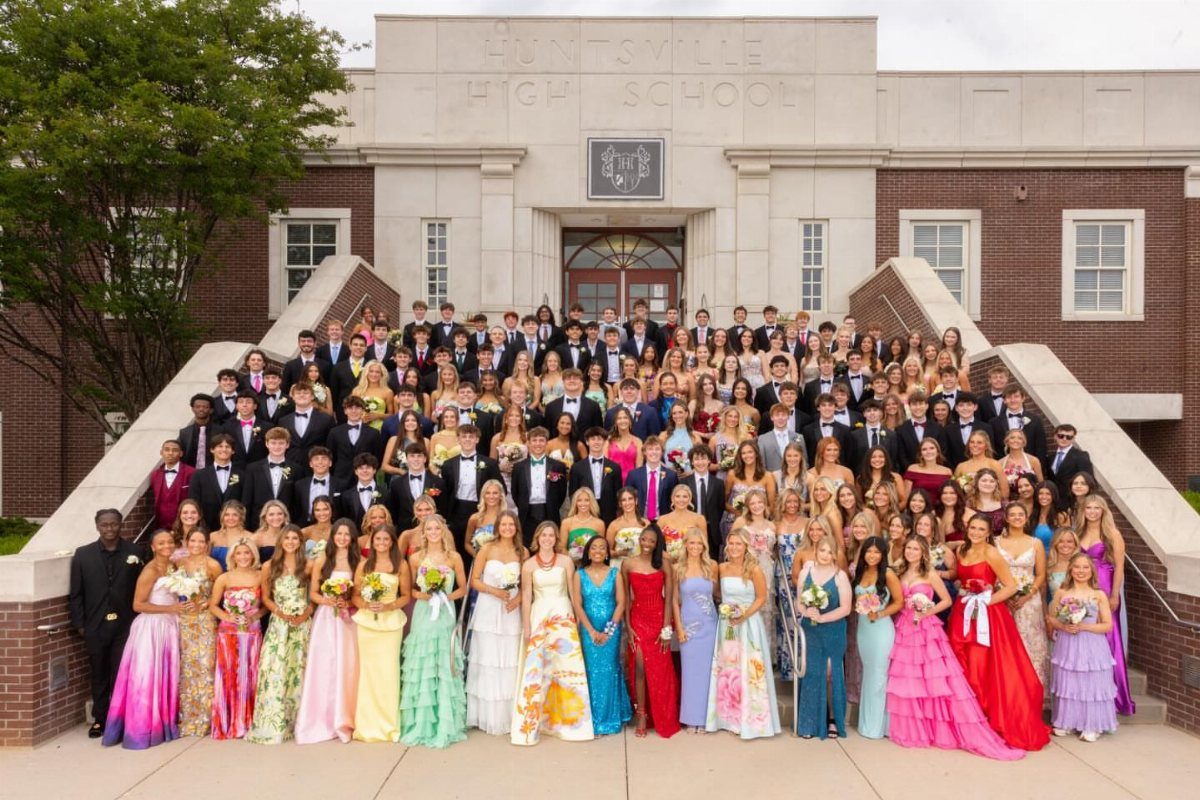 Large group of students in formal prom wear posing on school steps.