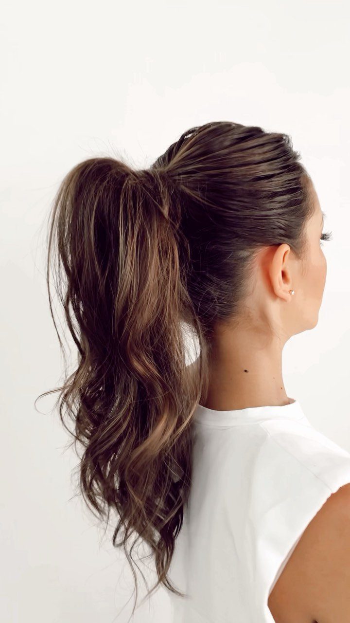 Woman with brown hair styled in a high curly ponytail wearing white shirt
