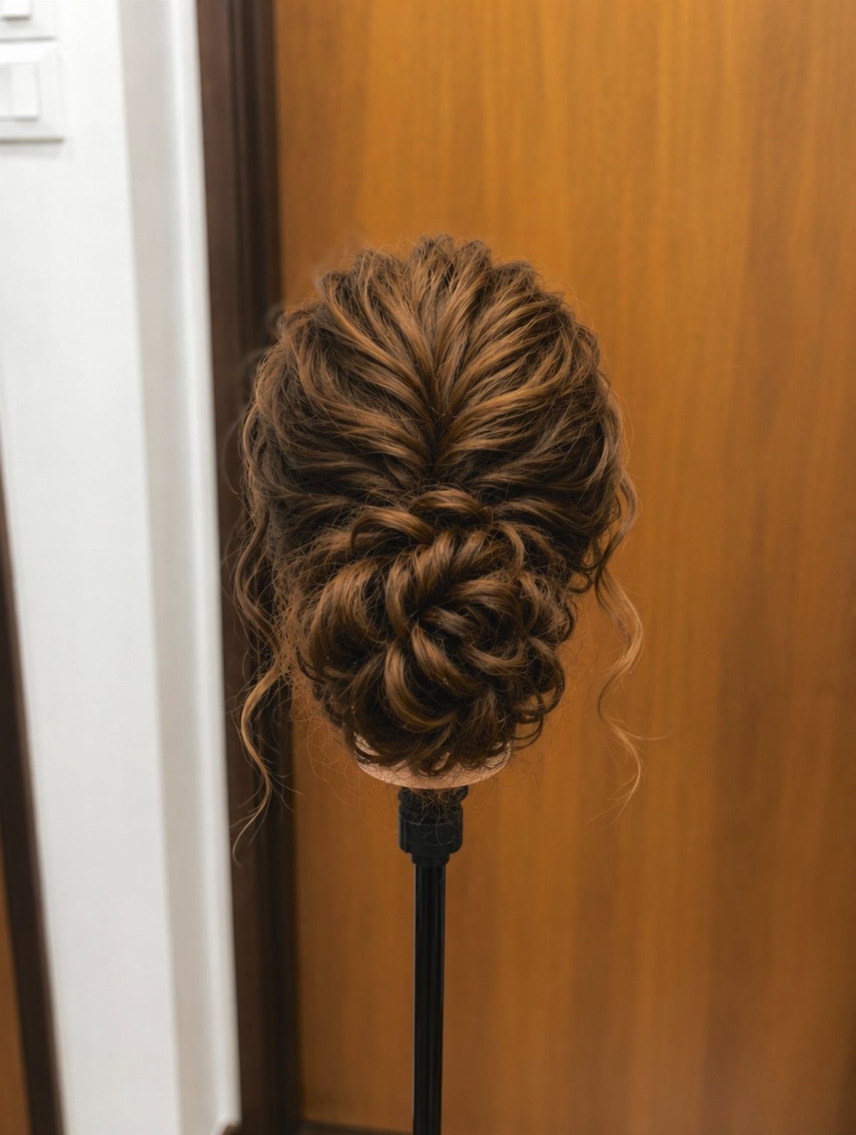 Intricate low messy bun updo on a brown-haired mannequin head.