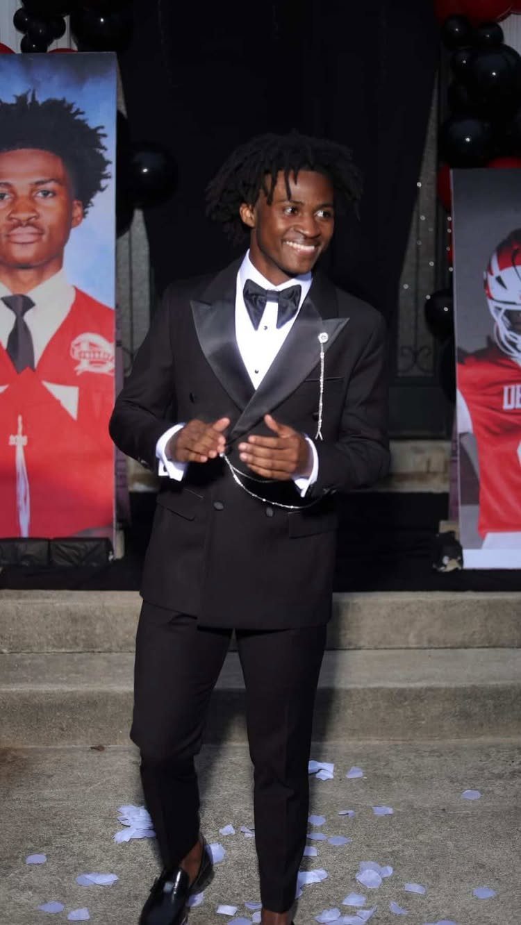 Young man smiling in a black tuxedo with a bow tie on concrete steps.