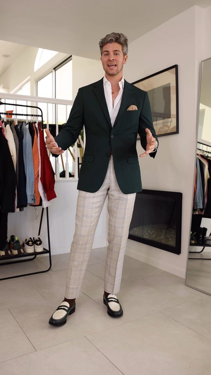 Man wearing a dark green blazer and light plaid trousers in a room.