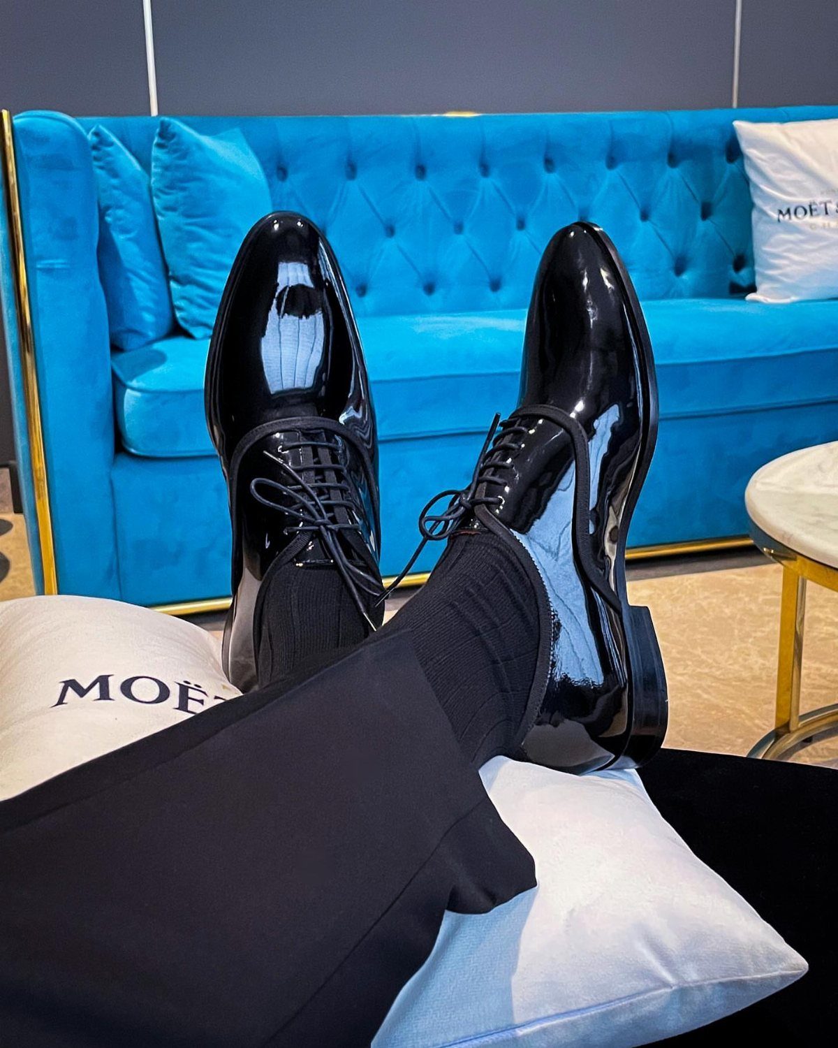 Shiny black patent leather dress shoes worn with black trousers and socks.