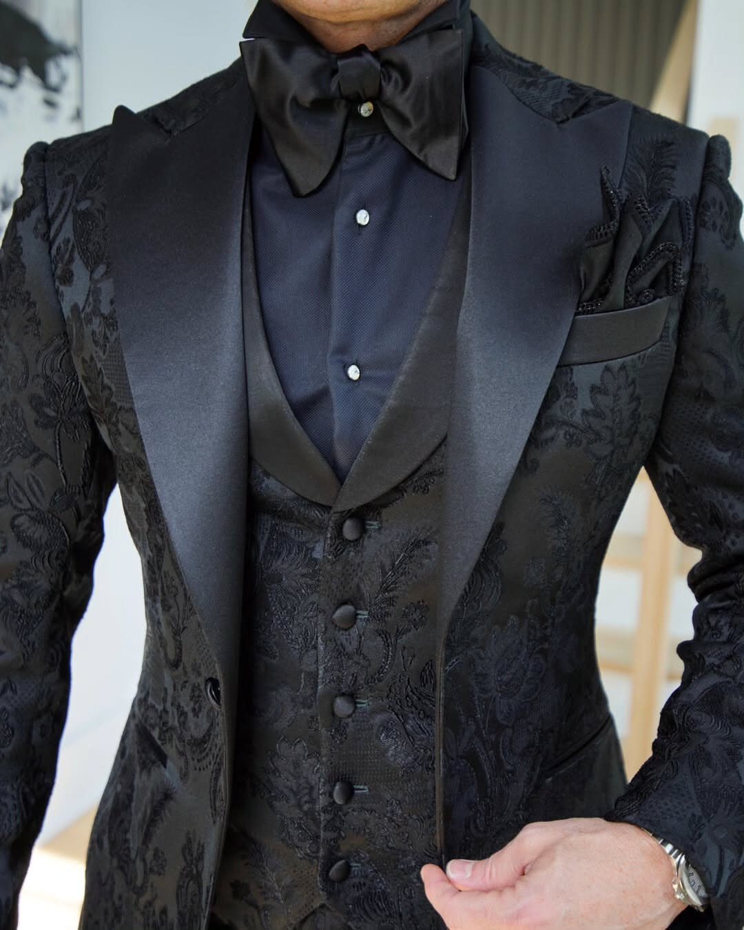 Man wearing a black patterned tuxedo with satin lapels and a black bow tie
