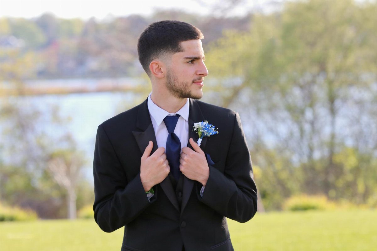Young man in a black suit and blue tie adjusting his jacket lapels.