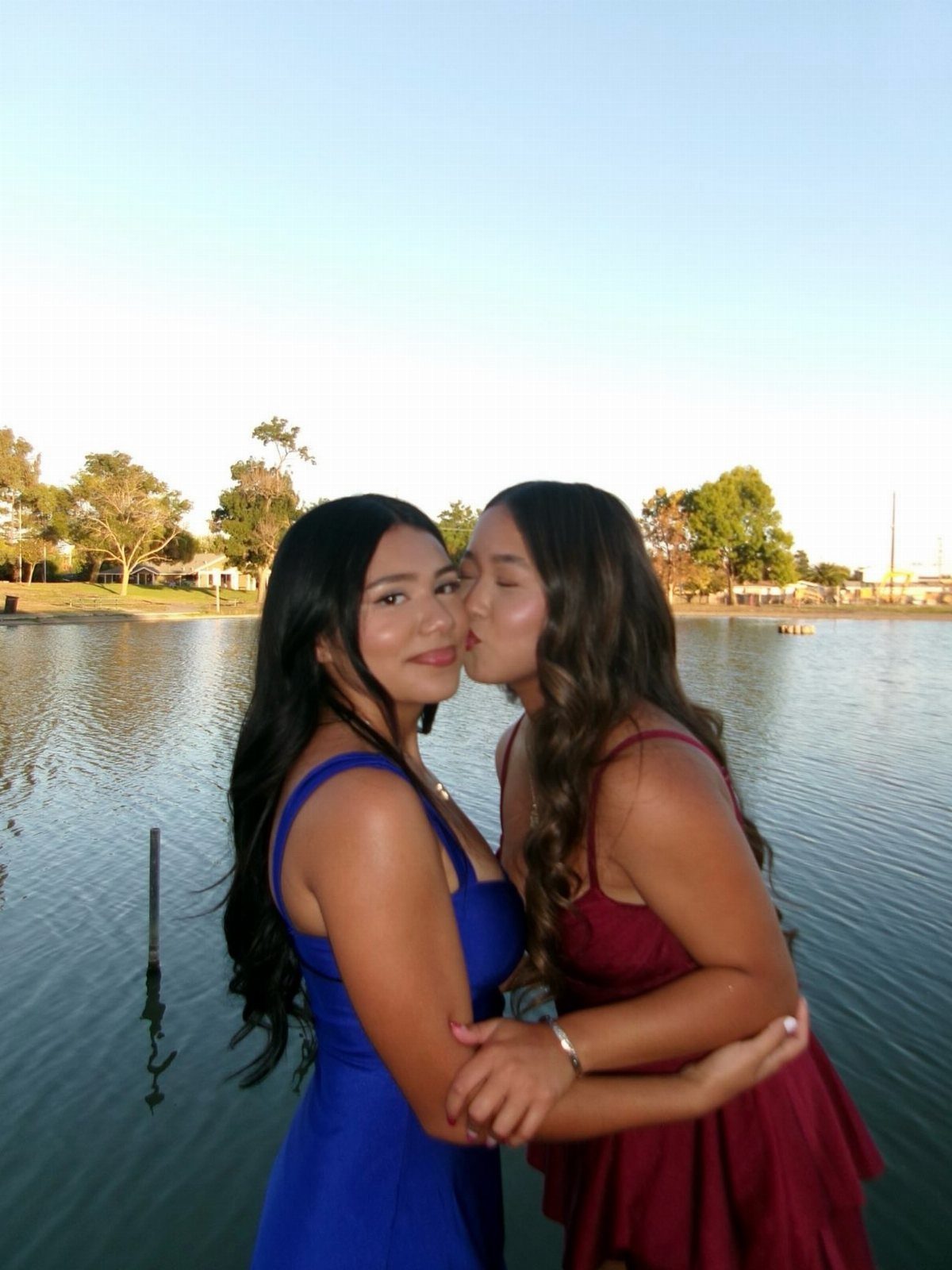 Two young women in formal dresses, one kissing the other on the cheek.