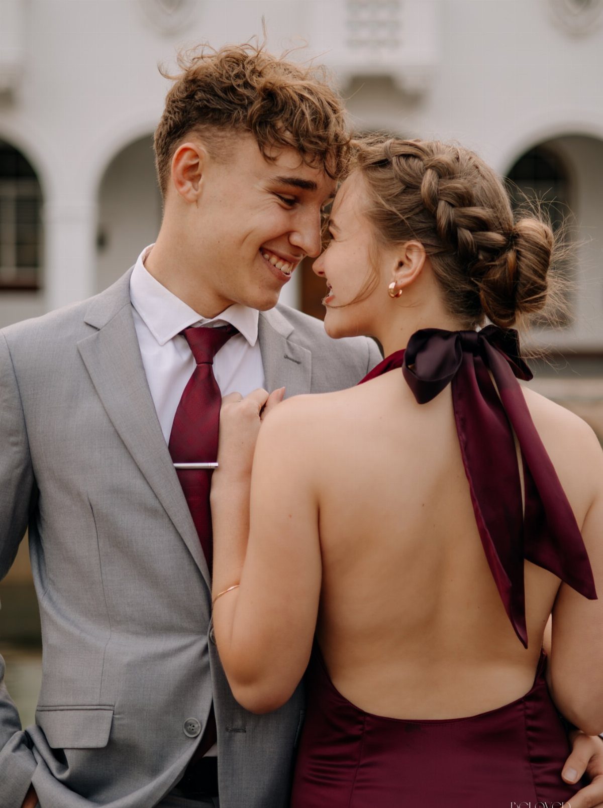 Young couple in formal wear smiling and looking at each other outdoors.