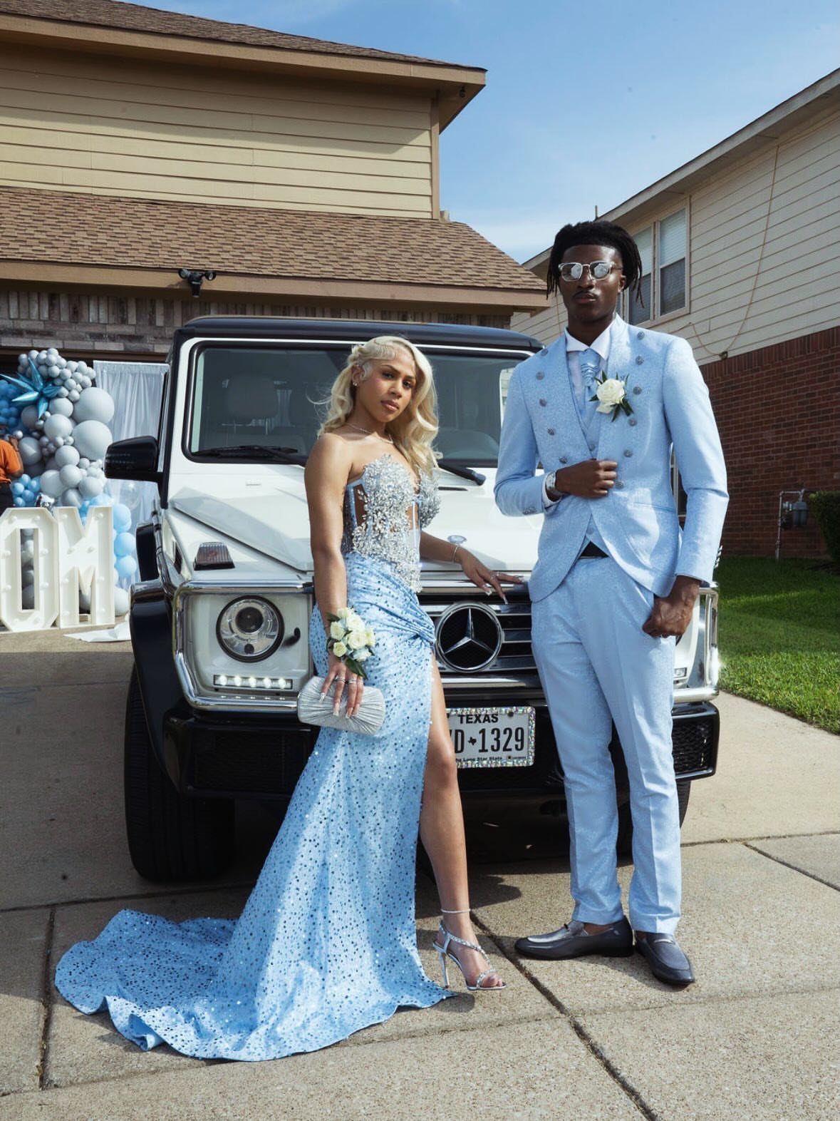Couple in light blue formal wear posing by a white luxury SUV.