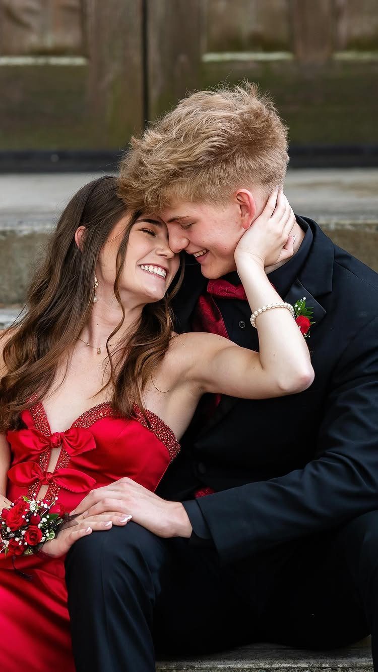 Young couple in red dress and black suit sitting close on concrete steps.