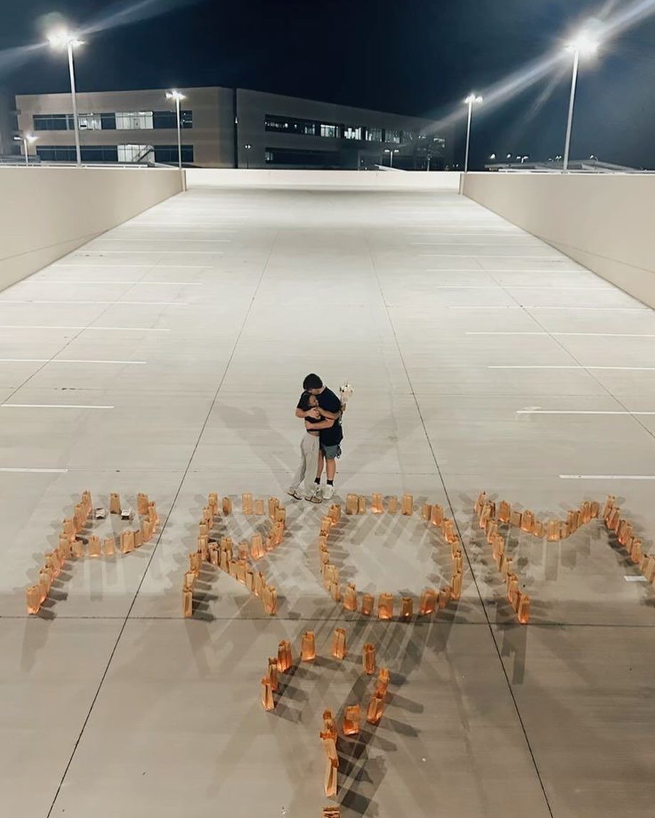 Couple hugging in a parking garage with candles spelling PROM? on the ground