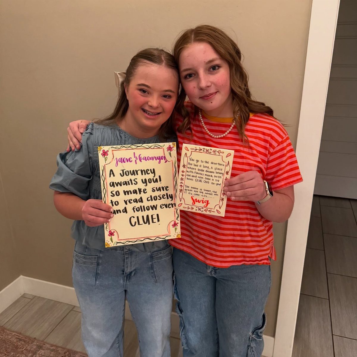 Two teenage girls holding handmade signs with clues for a prom proposal.