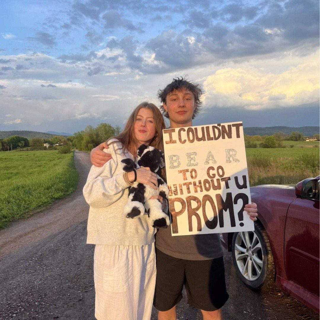 Young couple on a dirt road with a promposal poster and stuffed bear