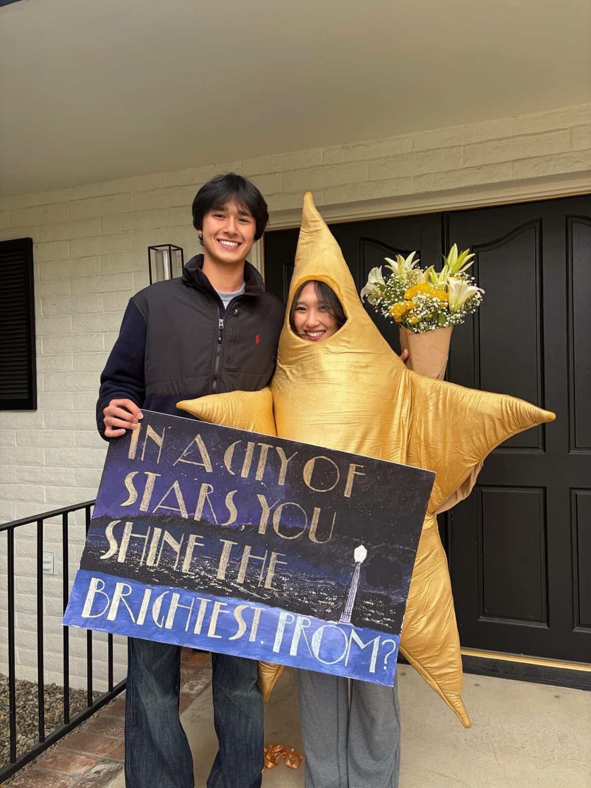Young man and woman in star costume holding a prom proposal poster outdoors
