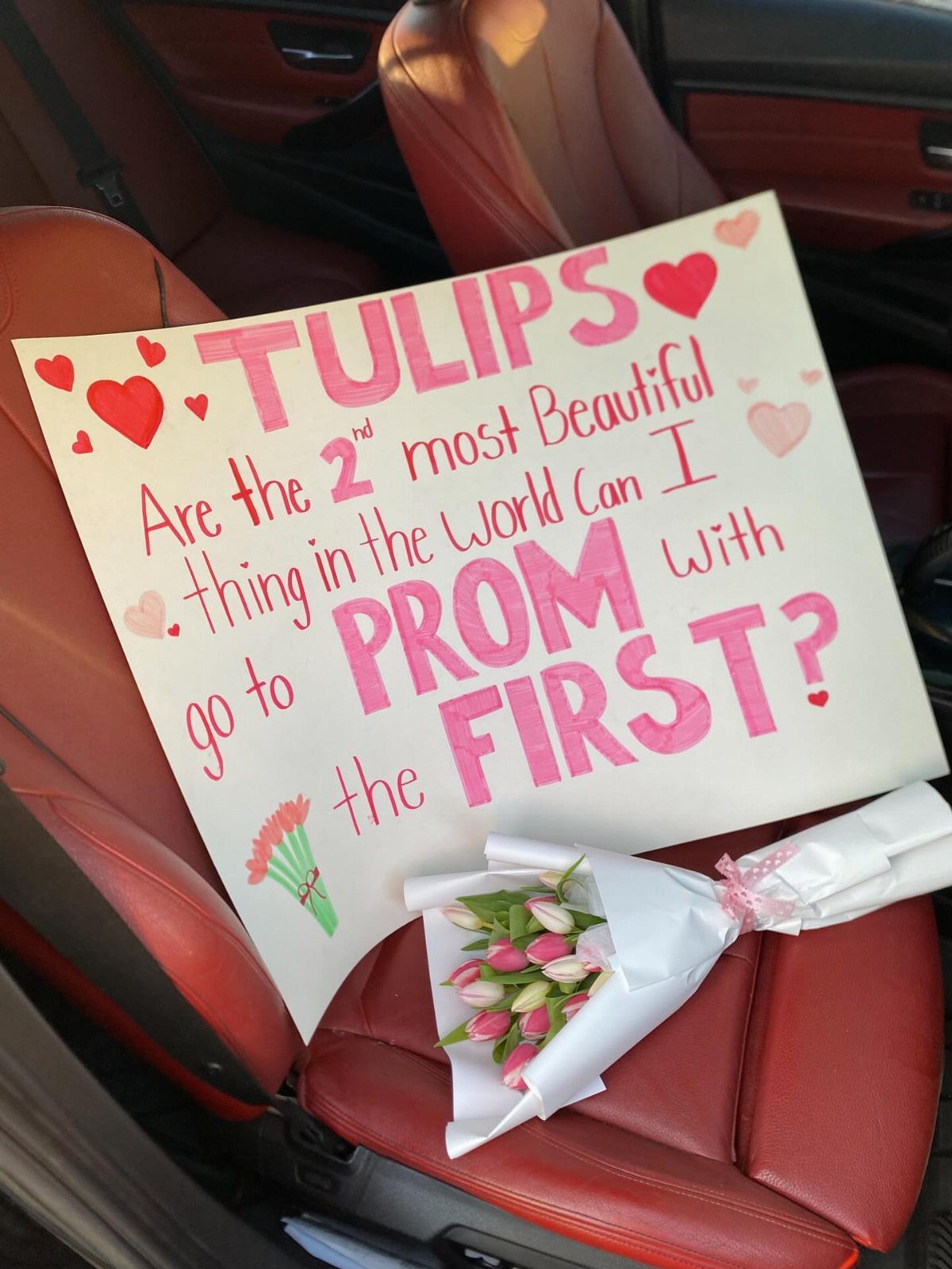 Prom proposal poster with tulips resting on red leather car seats.