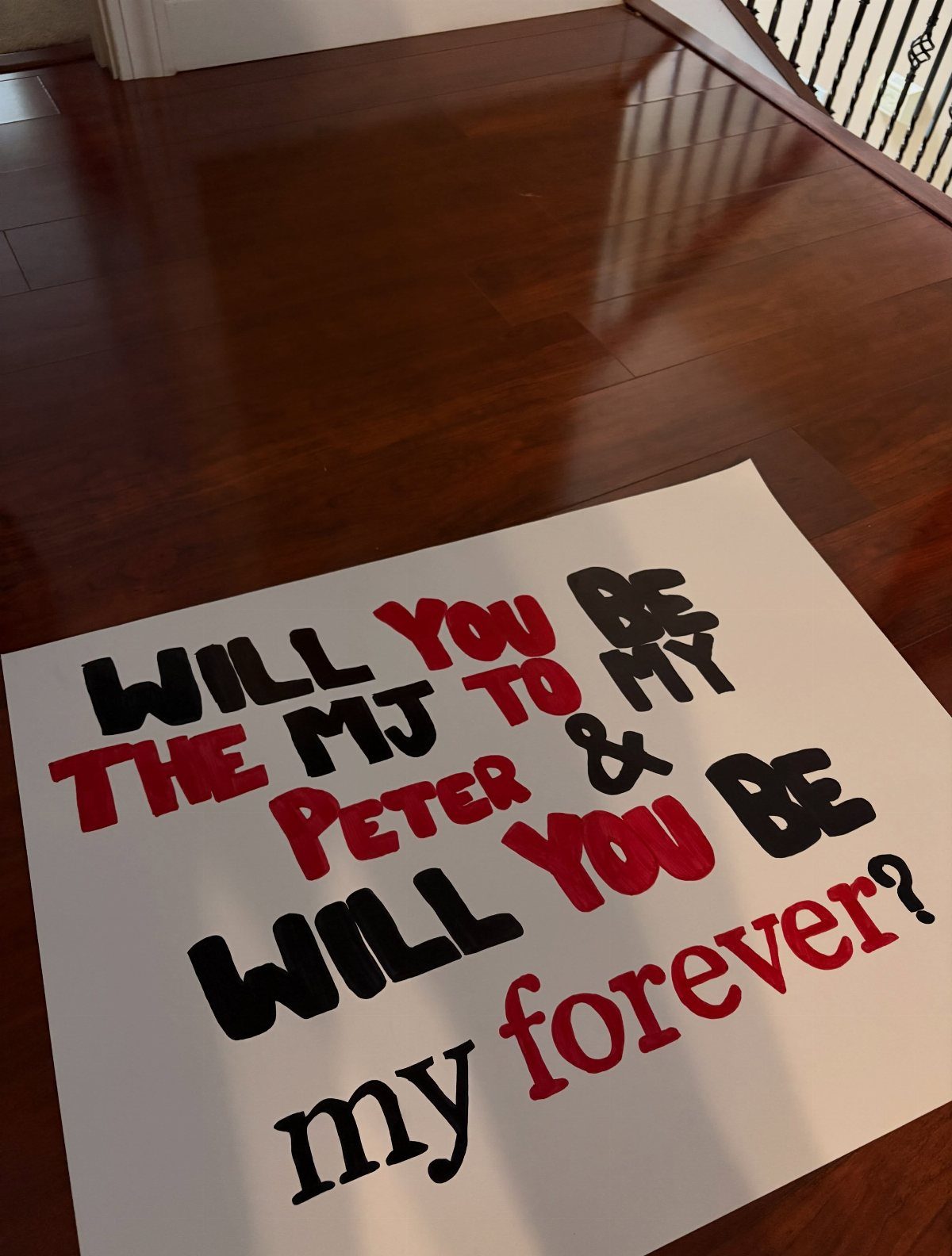 White poster board with red and black text on a wooden floor.