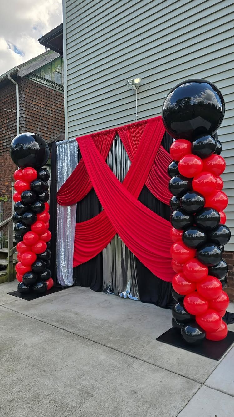Red and black balloon columns framing a draped fabric photo backdrop outdoors.