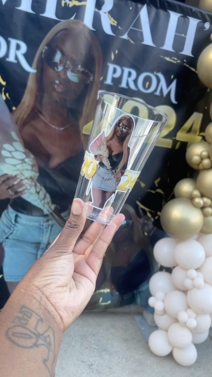 Clear plastic cup with personalized photo and 2024 text held before prom banner