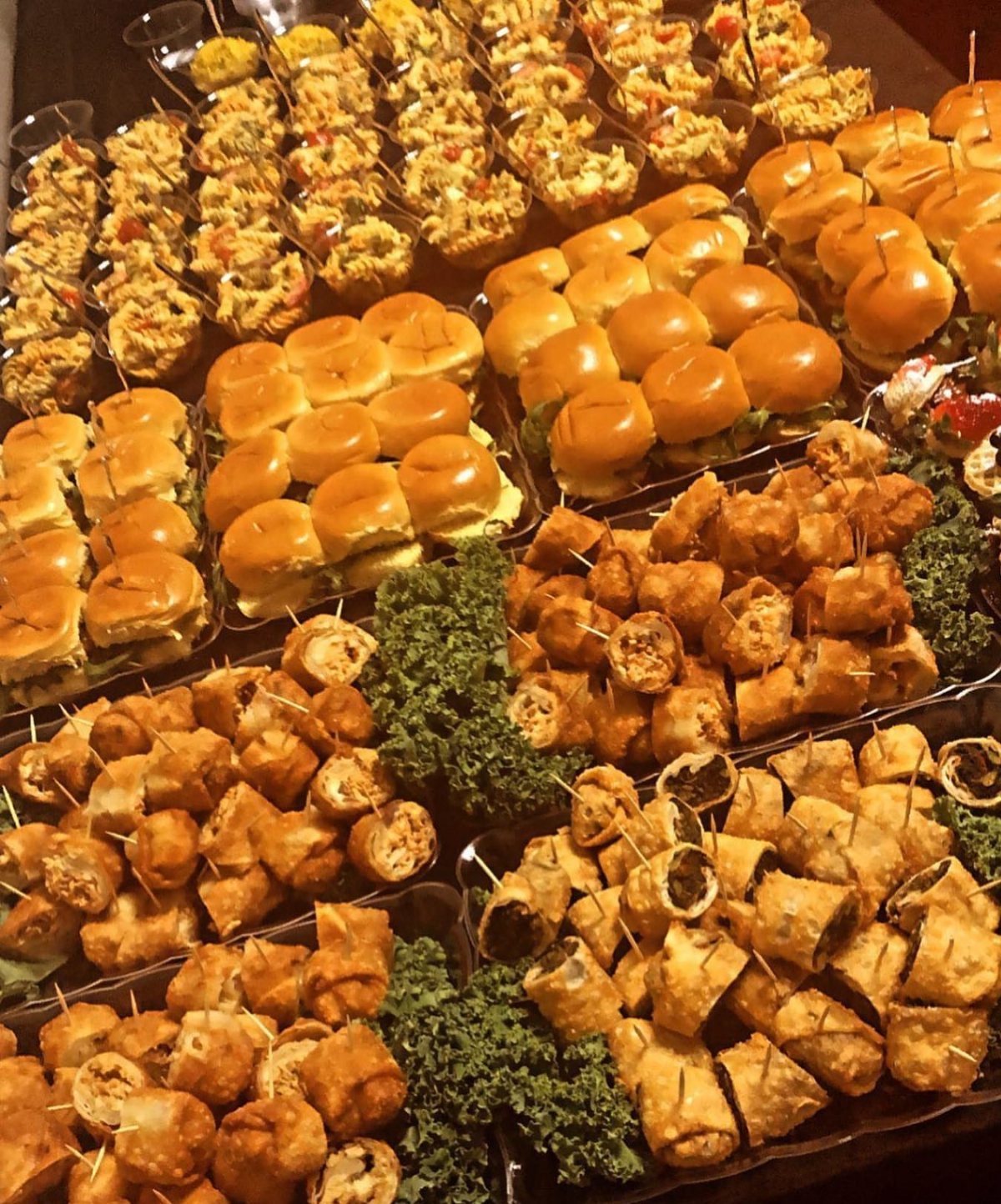 Assorted finger foods including mini sliders, spring rolls, and appetizer cups on platters.