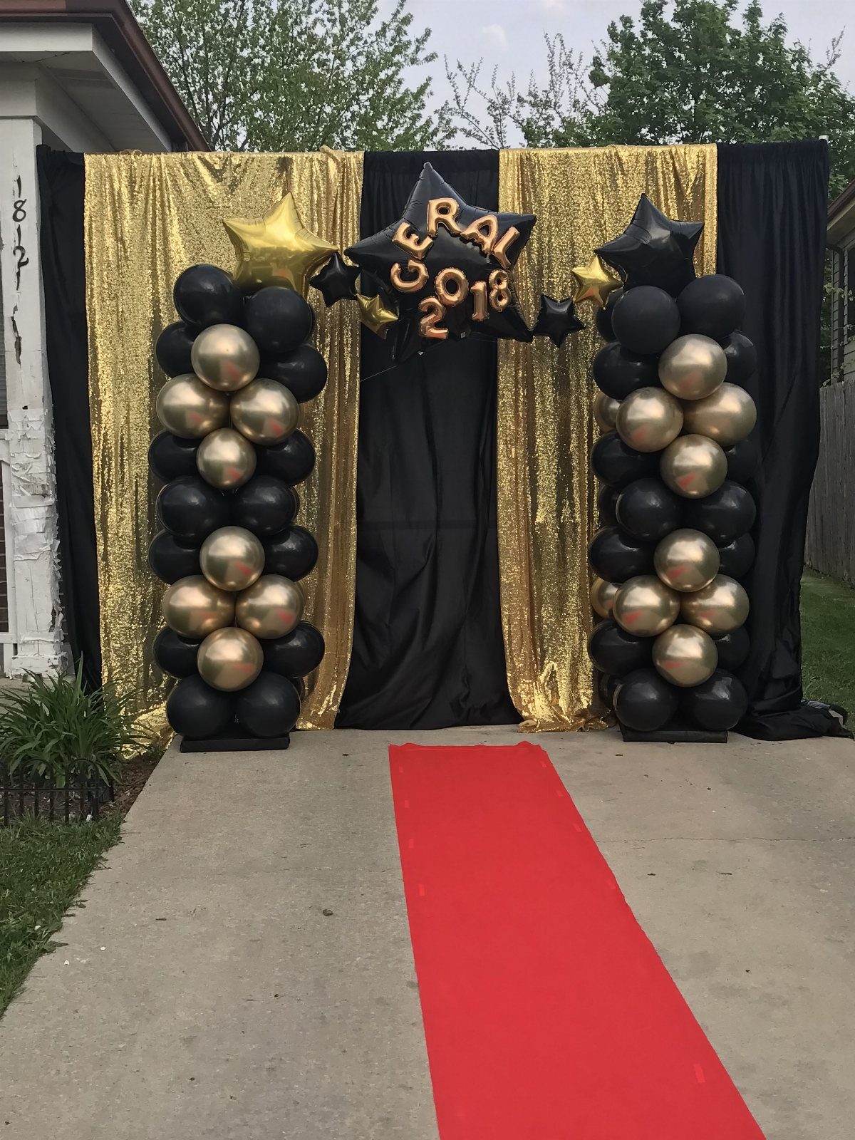Red carpet runner leading to gold and black balloon columns and sequin backdrop.