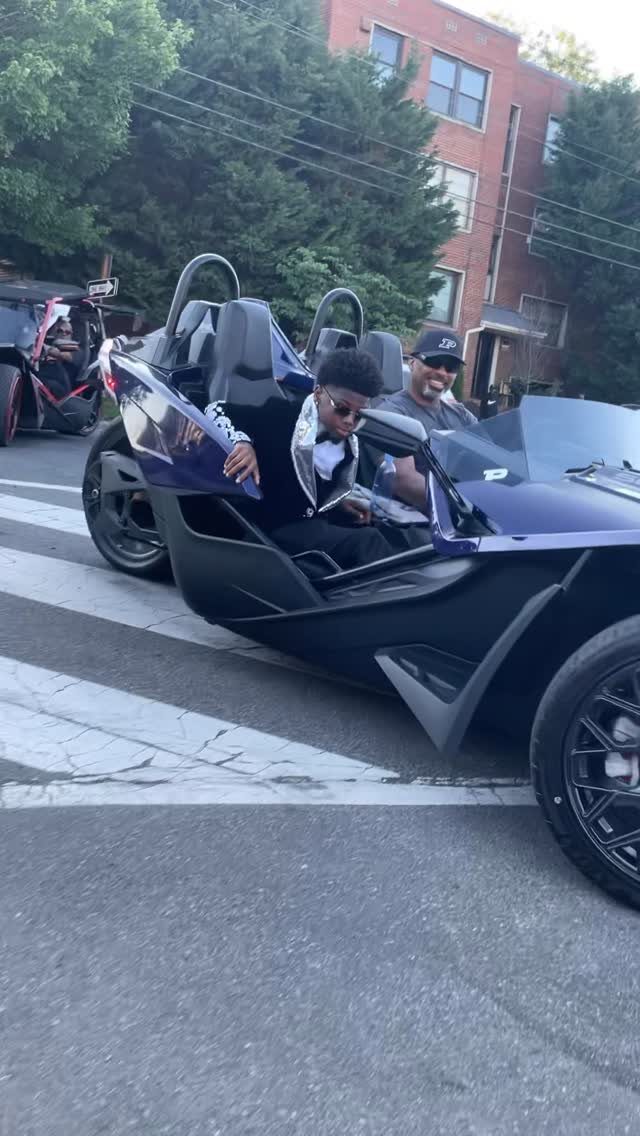 Young man in a tuxedo sitting in a purple three-wheeled prom vehicle.