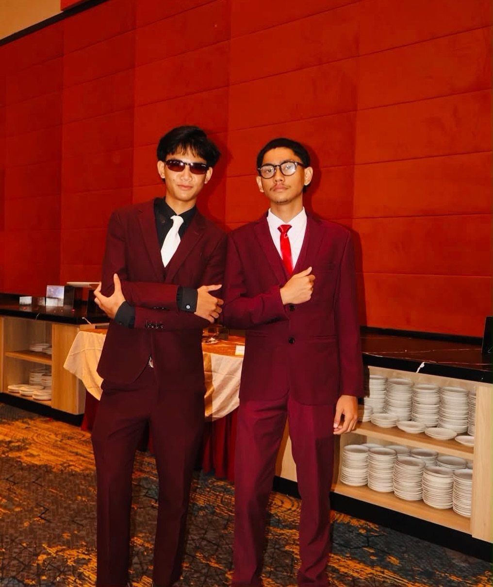 Two young men posing in burgundy maroon suits with sunglasses and ties.