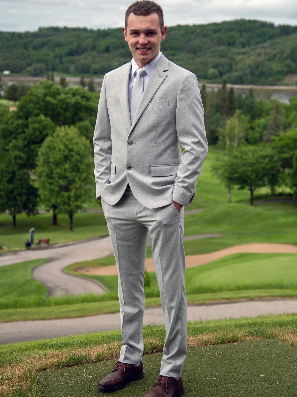 Young man wearing a light grey suit with a white tie outdoors.
