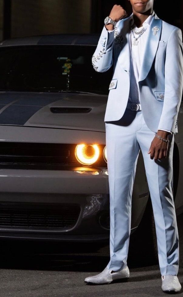 Man in a light blue suit posing next to a grey muscle car.