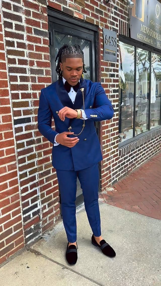 Young man in a royal blue suit and bow tie posing by brick wall