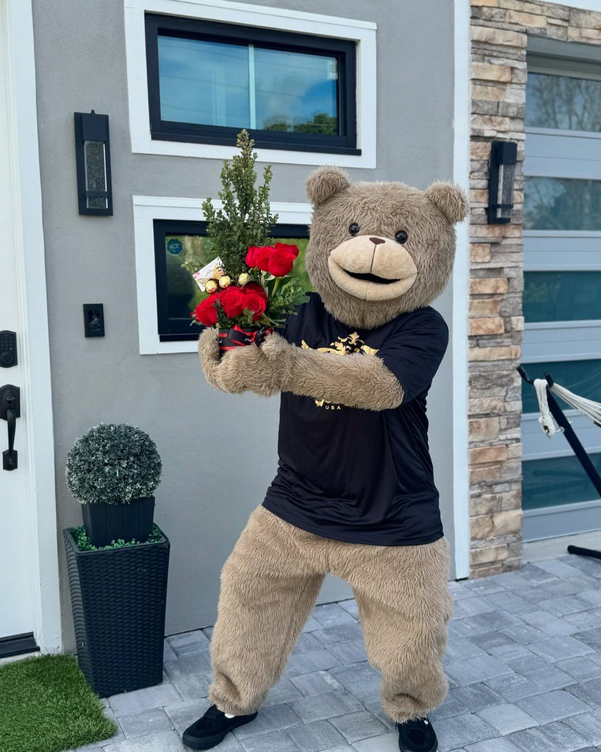 Person in teddy bear mascot costume holding a bouquet of red roses outdoors